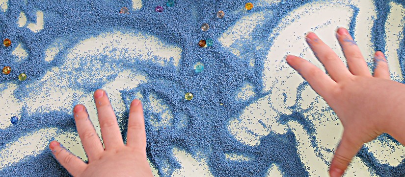 Kind malt in Sand, der auf einem Lichttisch verteilt ist